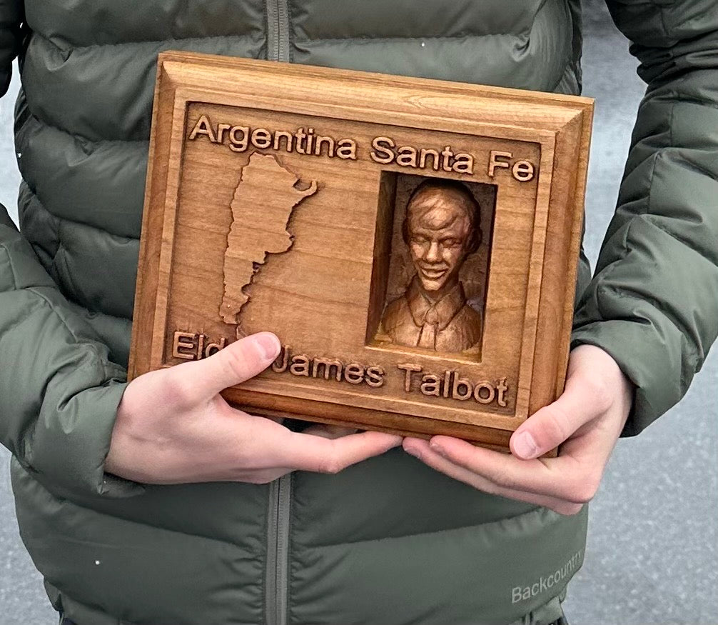 Wooden plaque with engraved text and a portrait, held by a New Missionary